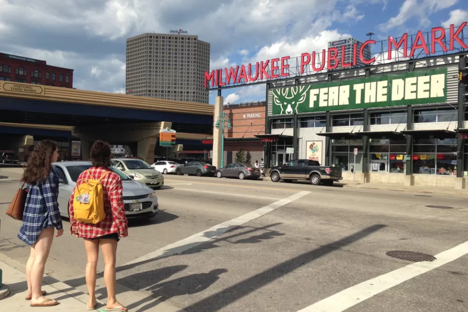 Two women waiting to cross street facing Milwaukee Public Market sign